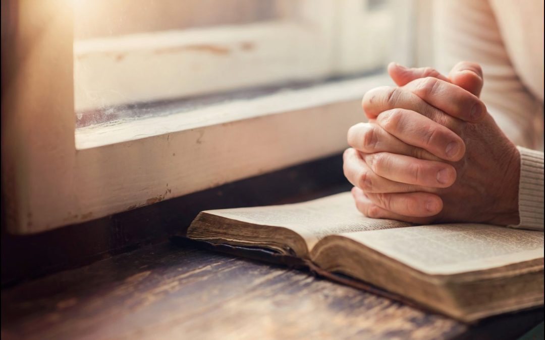 An open Bible, hands folded in prayer